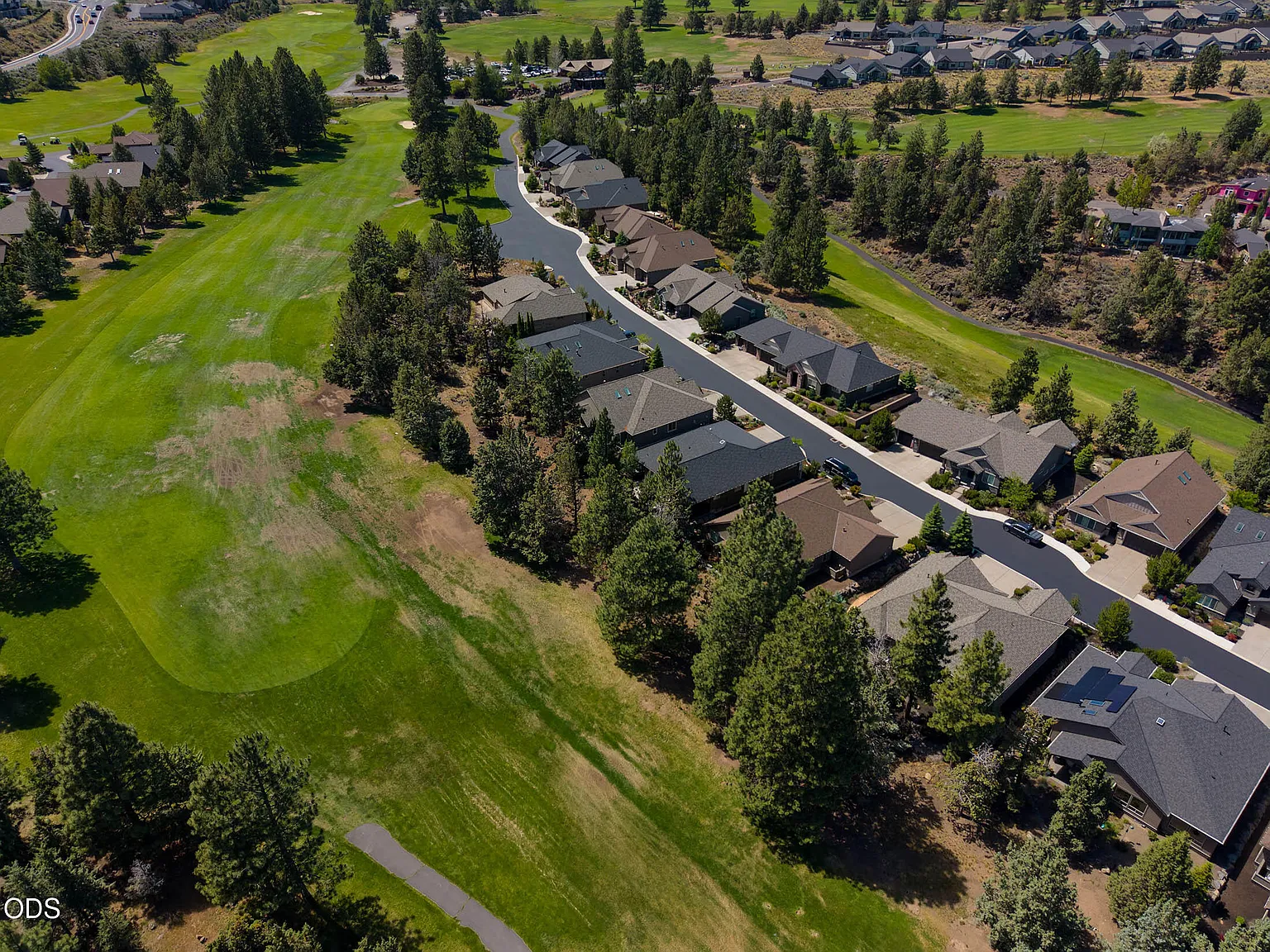 Aerial of the 18th fairway of Rivers Edge Golf Course, with a row of single-level homes lining the cart path and the green grass running along the property line of 2533 NW Pine Terrace