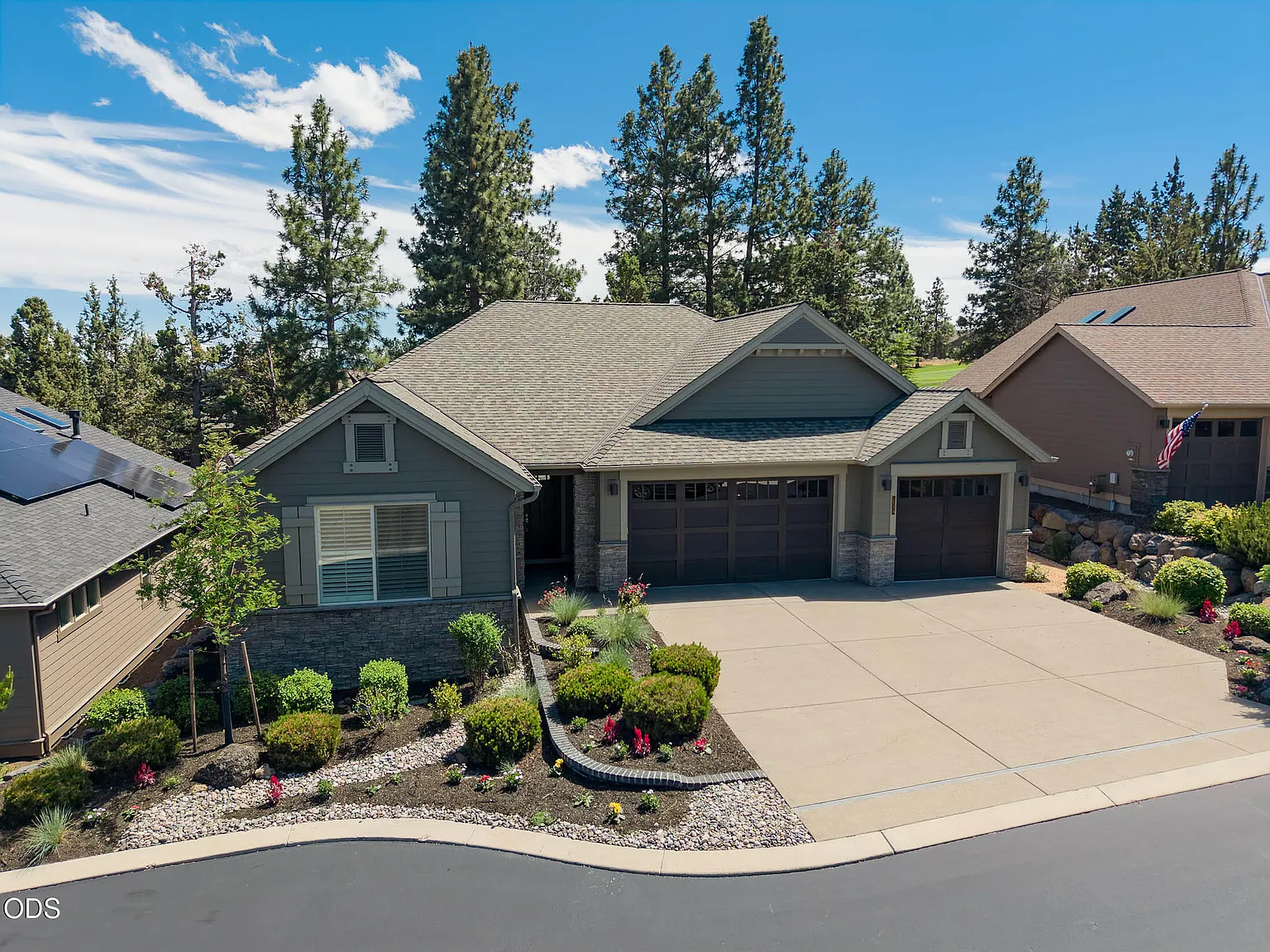 Elevated front view of 2533 NW Pine Terrace, a Pacific Northwest Craftsman with stone-pillared entry, shingle roof, and board-and-batten gables framed by ponderosa pines under a Bend sky